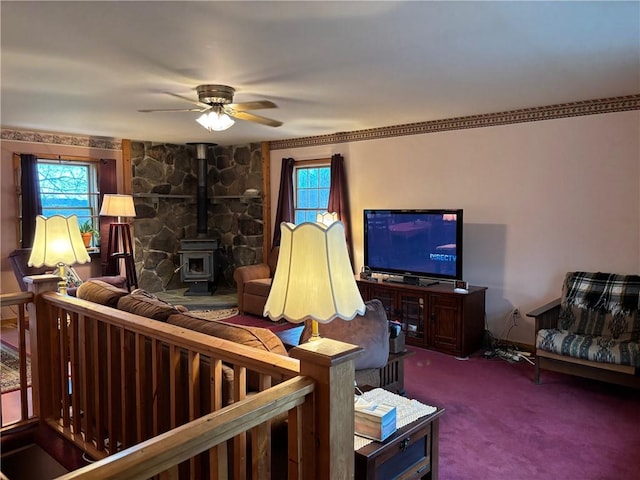 carpeted living area with a wood stove, a ceiling fan, and plenty of natural light