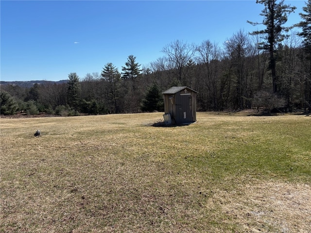 view of yard with a storage shed, a wooded view, and an outdoor structure