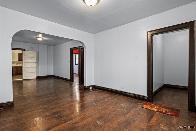 unfurnished room with arched walkways, wood finished floors, and baseboards