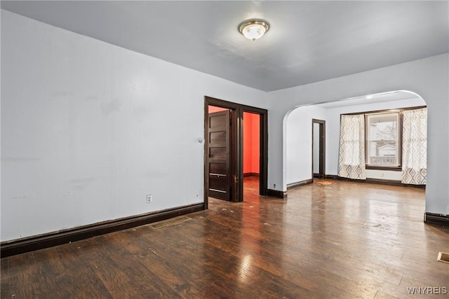 spare room featuring baseboards, arched walkways, and wood finished floors
