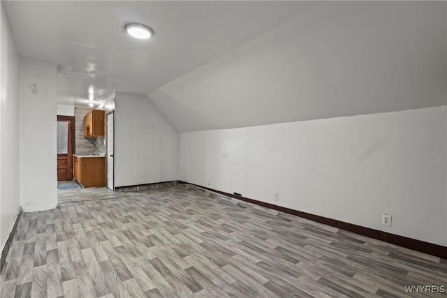 additional living space with light wood-style flooring, vaulted ceiling, and baseboards