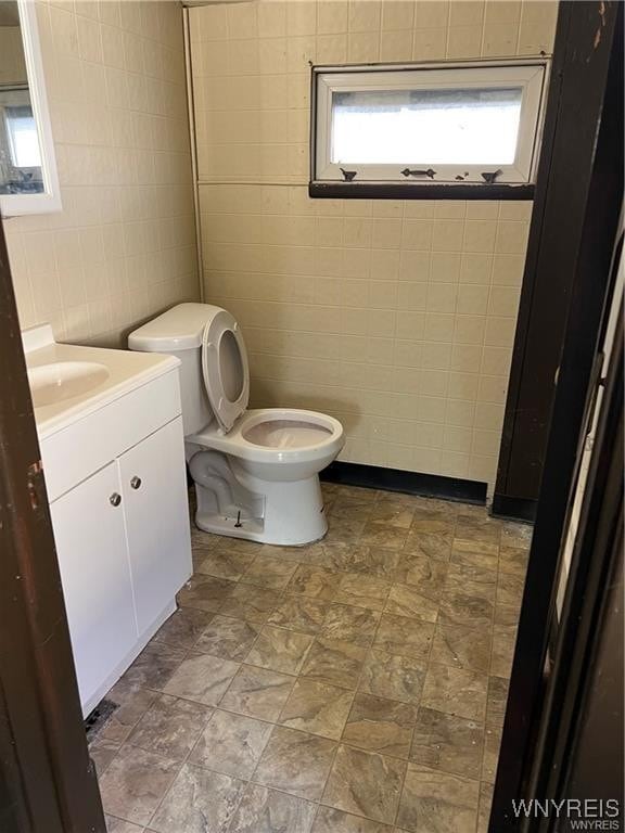 bathroom with toilet, vanity, and tile walls