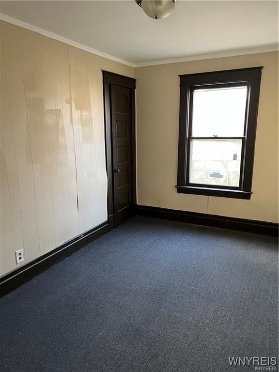 empty room featuring crown molding, dark colored carpet, and baseboards