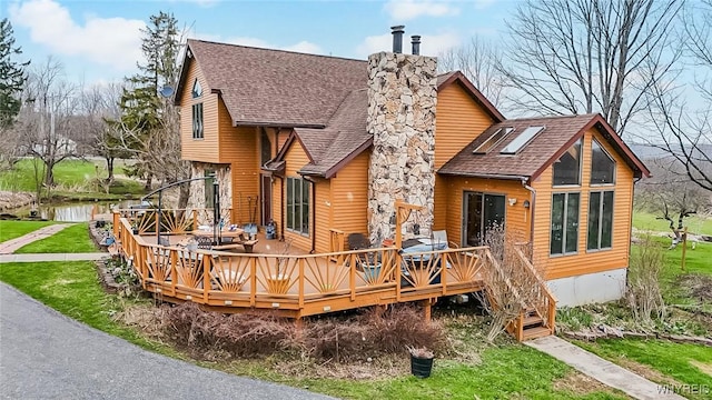 back of property with roof with shingles, a wooden deck, and a chimney