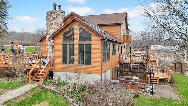 view of side of property with a wooden deck, stairs, a chimney, and a hot tub