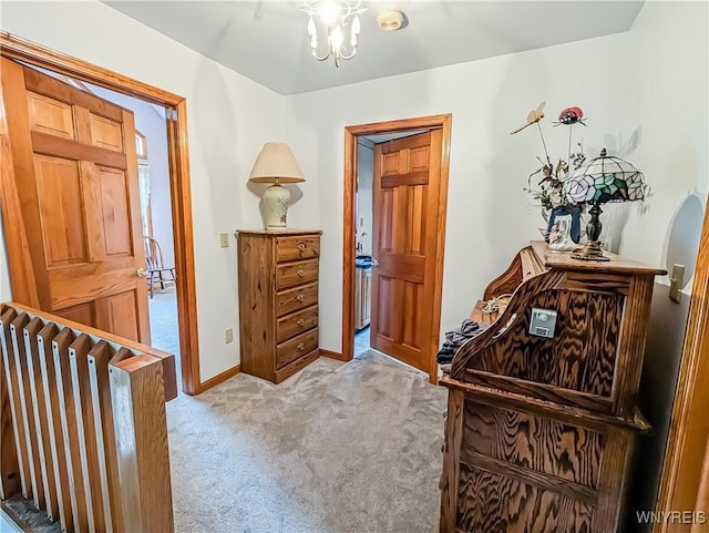 hall featuring baseboards, carpet, and a chandelier