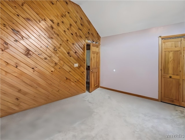 spare room featuring wood walls, baseboards, vaulted ceiling, and light carpet
