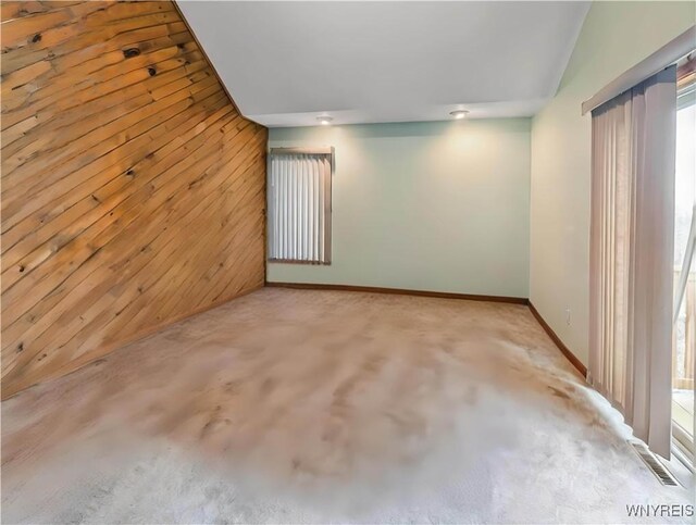 spare room featuring baseboards, vaulted ceiling, wood walls, and visible vents