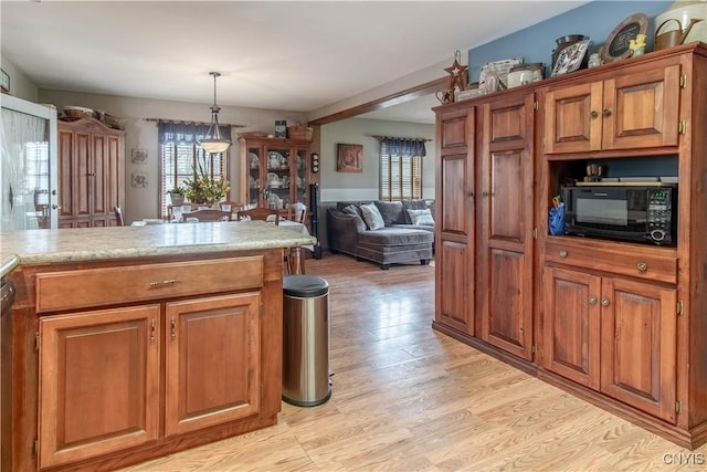 kitchen with brown cabinetry, light wood-type flooring, black microwave, light countertops, and pendant lighting