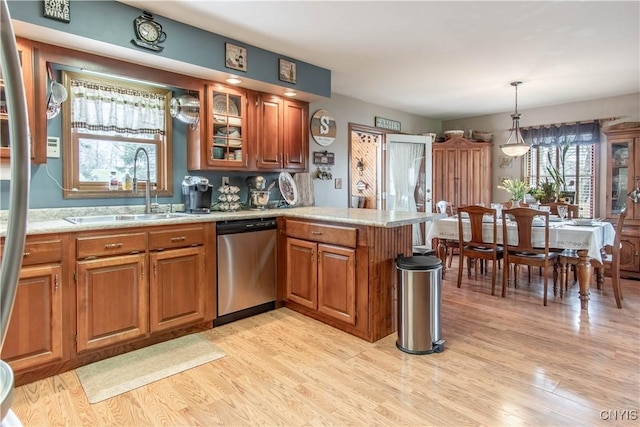 kitchen with brown cabinetry, stainless steel dishwasher, a peninsula, and a sink
