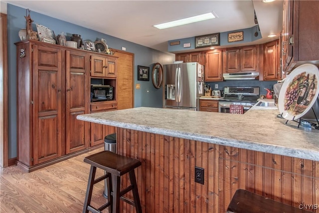 kitchen featuring under cabinet range hood, light wood-style floors, a peninsula, light countertops, and appliances with stainless steel finishes