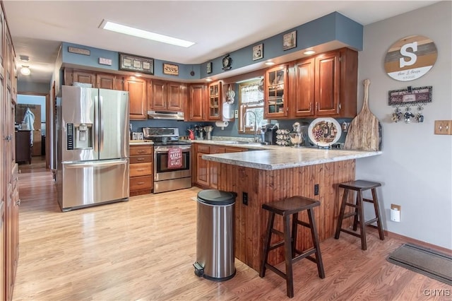 kitchen with light wood-style flooring, a sink, stainless steel appliances, under cabinet range hood, and a peninsula