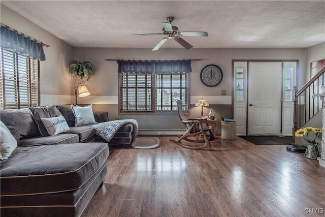 living area with a baseboard heating unit, ceiling fan, stairs, a textured ceiling, and wood finished floors