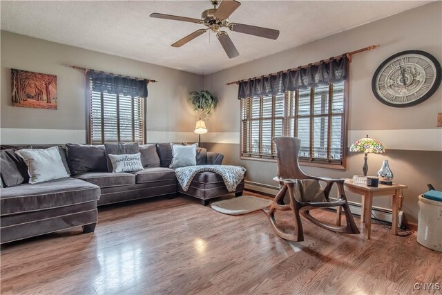 living room featuring wood finished floors, a baseboard heating unit, ceiling fan, and plenty of natural light