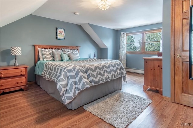 bedroom featuring a baseboard heating unit, light wood finished floors, and vaulted ceiling