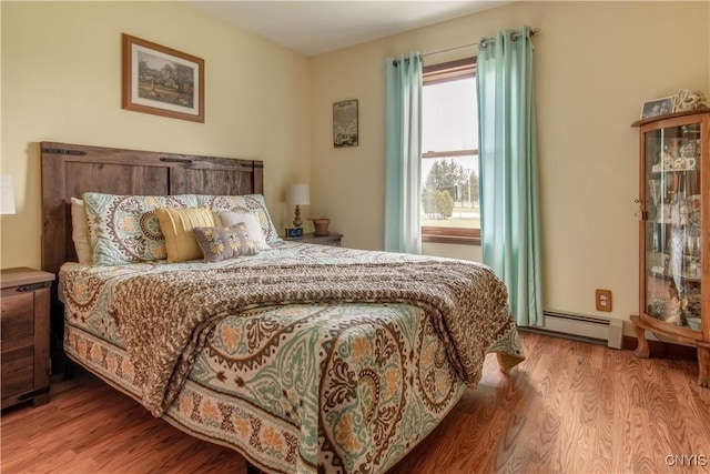 bedroom with wood finished floors and a baseboard heating unit