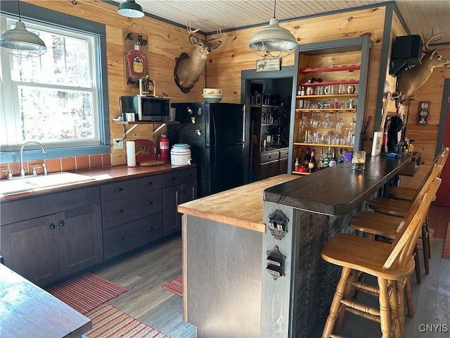 kitchen with a sink, stainless steel microwave, freestanding refrigerator, and wooden walls