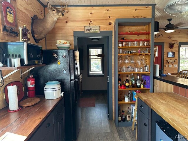 kitchen with wooden counters, freestanding refrigerator, ceiling fan, wooden walls, and wood finished floors