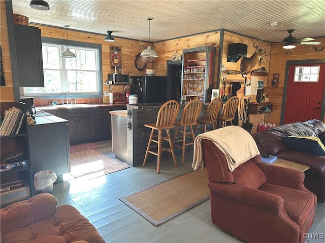 living room featuring wood walls, light wood-style flooring, a ceiling fan, and wood ceiling