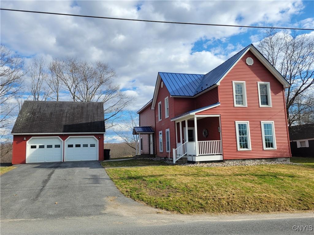 view of front of home with a detached garage, a porch, metal roof, an outdoor structure, and a front lawn
