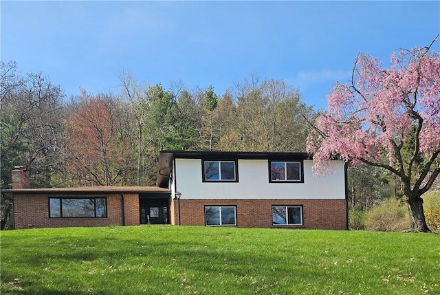view of front of house with a chimney, brick siding, and a front lawn