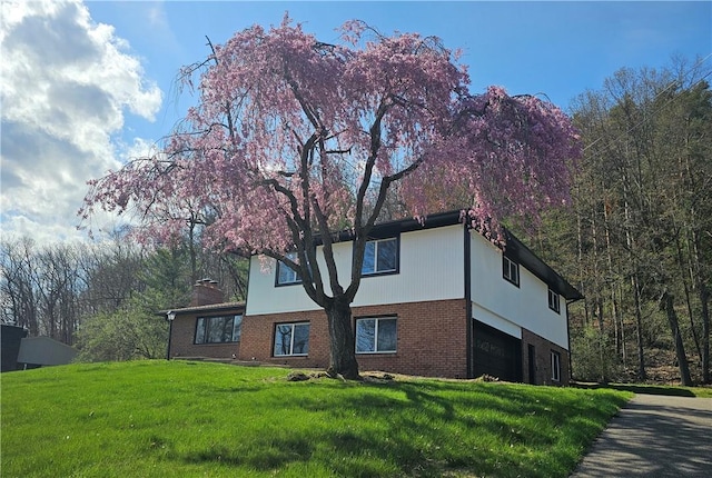 view of side of home featuring a garage, brick siding, a chimney, and a lawn