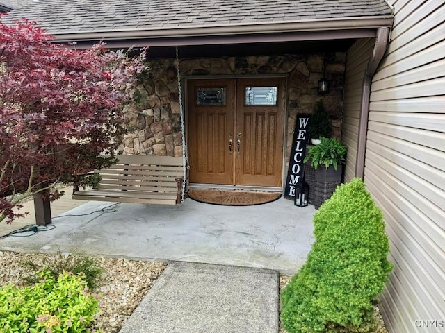 doorway to property with roof with shingles and stone siding