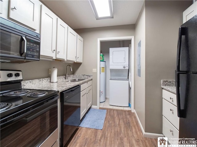 kitchen featuring white cabinets, a sink, stacked washer / dryer, black appliances, and light wood finished floors