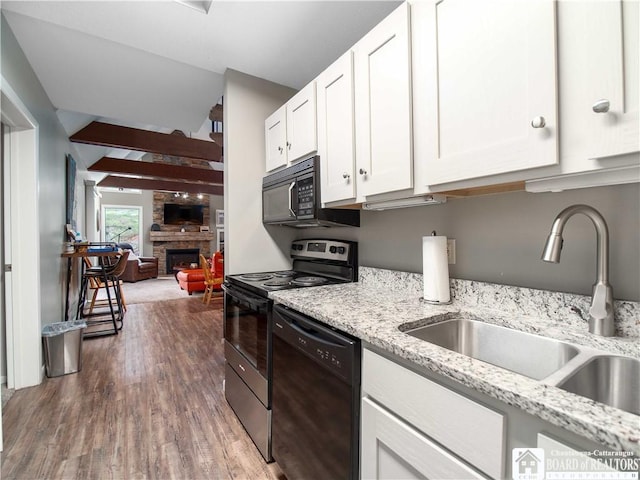kitchen with a large fireplace, white cabinets, black appliances, wood finished floors, and a sink