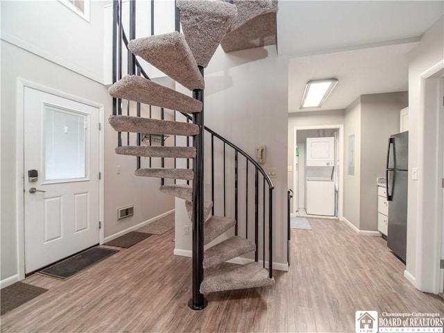 staircase with stacked washer and dryer, visible vents, baseboards, and wood finished floors