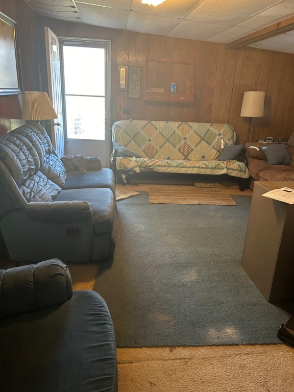 living room featuring a paneled ceiling, wooden walls, and carpet floors