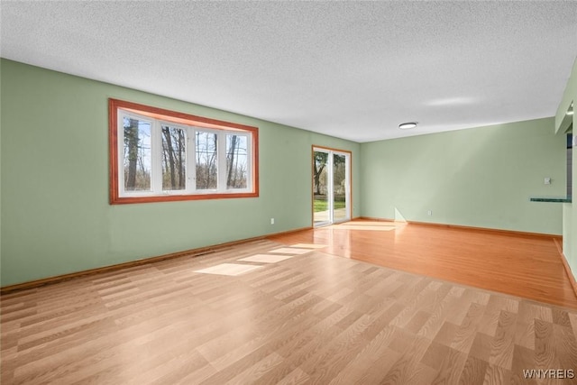 empty room featuring light wood-style floors, a textured ceiling, and baseboards