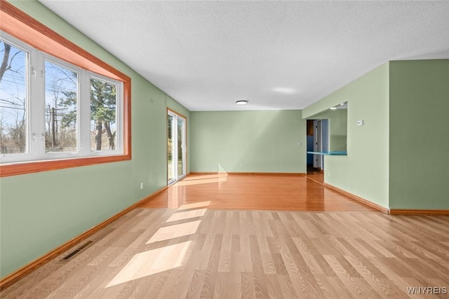 unfurnished room featuring visible vents, light wood-type flooring, baseboards, and a textured ceiling