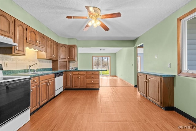 kitchen featuring white appliances, brown cabinetry, a peninsula, under cabinet range hood, and a sink
