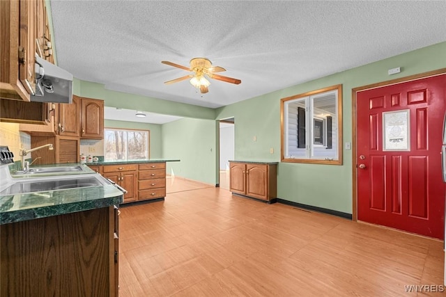 kitchen featuring ceiling fan, brown cabinetry, a textured ceiling, a sink, and dark countertops