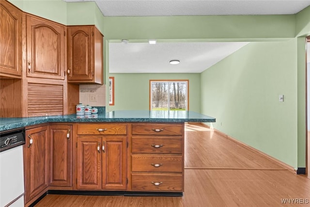 kitchen featuring tasteful backsplash, brown cabinetry, a peninsula, and dishwasher