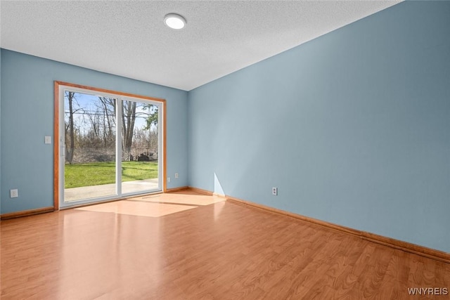 unfurnished room with a textured ceiling, wood finished floors, and baseboards