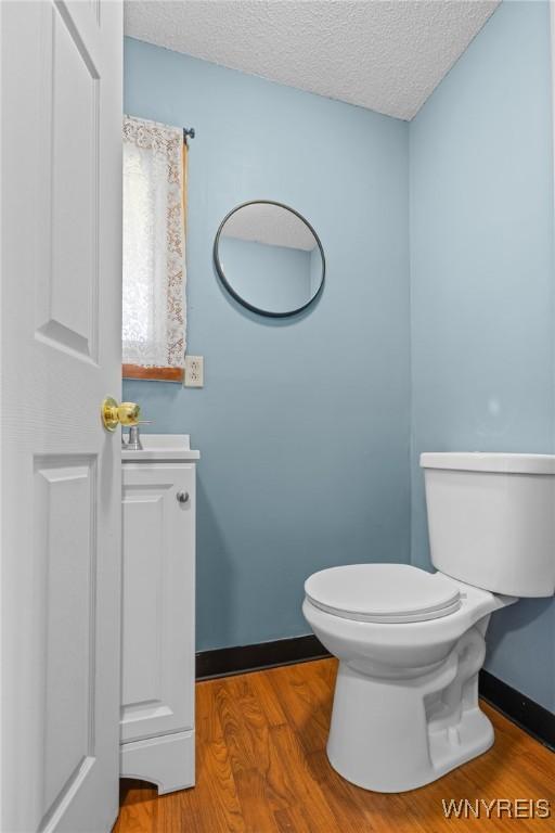 half bath featuring a textured ceiling, vanity, toilet, wood finished floors, and baseboards