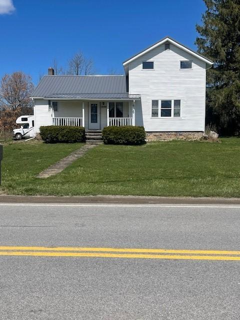 view of front of house featuring a chimney, a porch, a front lawn, and metal roof