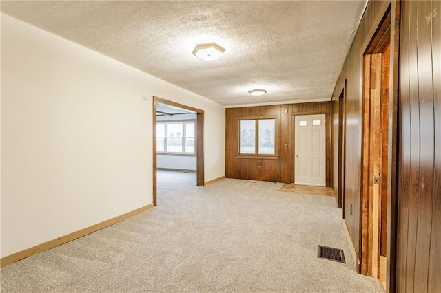 foyer with wooden walls, visible vents, light carpet, baseboards, and a textured ceiling