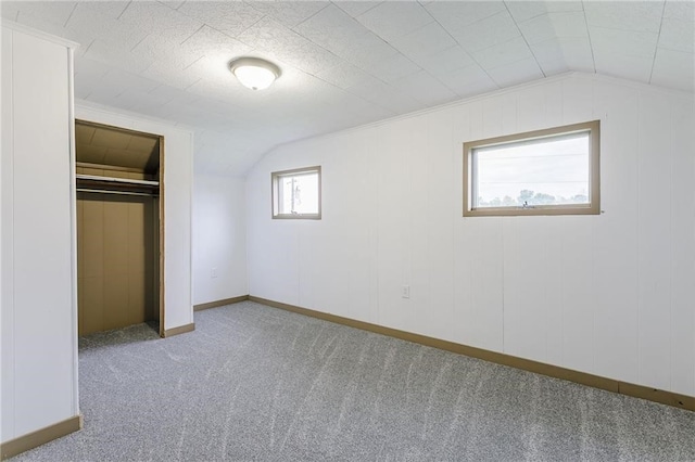 unfurnished bedroom featuring a closet, carpet flooring, lofted ceiling, and baseboards