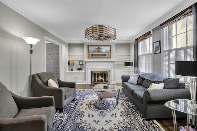 living room featuring built in features, ornamental molding, a glass covered fireplace, recessed lighting, and wood finished floors