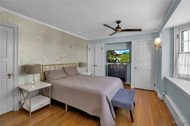 bedroom featuring two closets, a ceiling fan, baseboard heating, wood finished floors, and baseboards