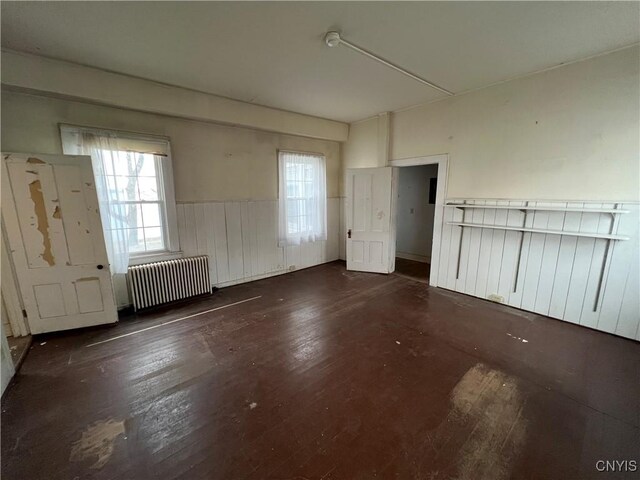 spare room with wood-type flooring, radiator heating unit, and a wainscoted wall