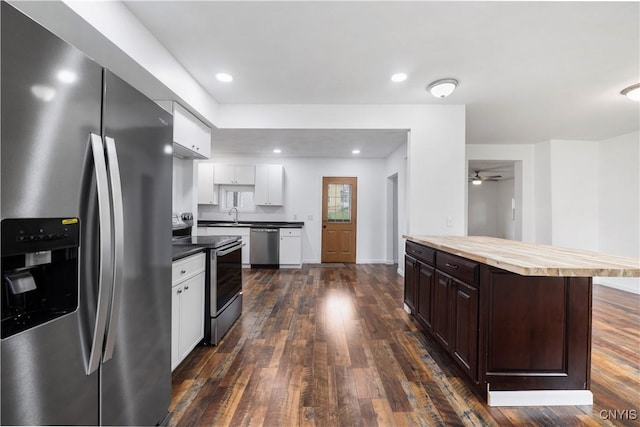 kitchen with appliances with stainless steel finishes, a sink, butcher block counters, white cabinetry, and dark wood-type flooring