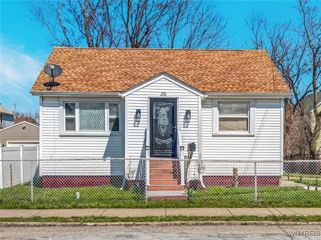 bungalow-style home featuring a detached garage, a shingled roof, and a fenced front yard