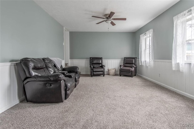 sitting room featuring carpet floors, a wainscoted wall, and a ceiling fan