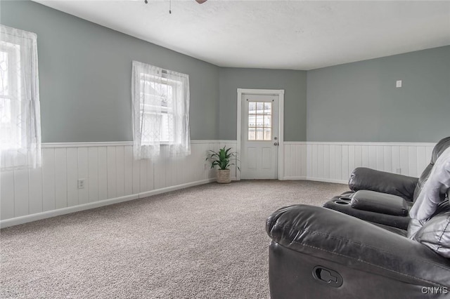 living area featuring carpet flooring, a ceiling fan, and a wainscoted wall