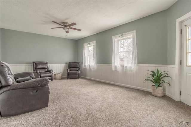 carpeted living room with a ceiling fan and a wainscoted wall