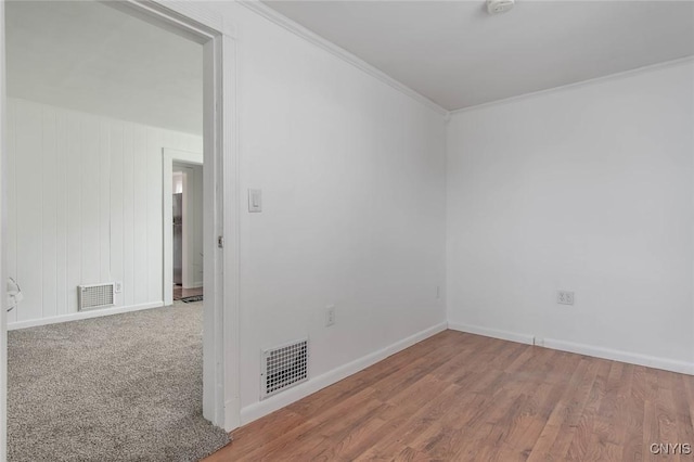empty room featuring crown molding, wood finished floors, baseboards, and visible vents